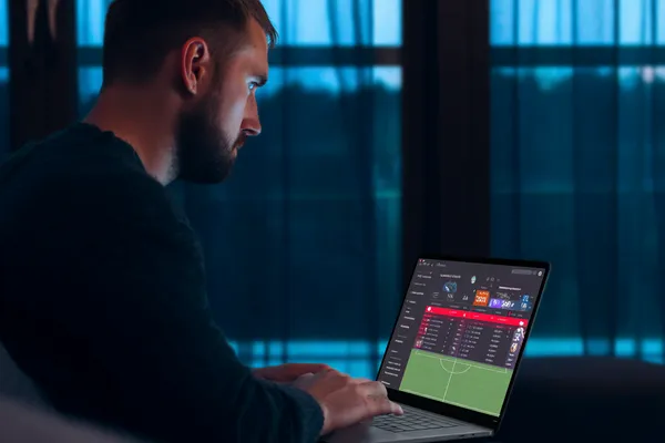 BDOK মোবাইল অ্যাপ — ক্যাসিনো ও স্পোর্টসের সম্পূর্ণ হাব একজন পুরুষ তার ল্যাপটপে মনোযোগ দিয়ে কাজ করছেন, ব্যাকগ্রাউন্ডে লাইভ স্ট্যাটস — যা BDOK মোবাইল অ্যাপের স্পোর্টস ও গেমিং ফিচারগুলোকে তুলে ধরে।